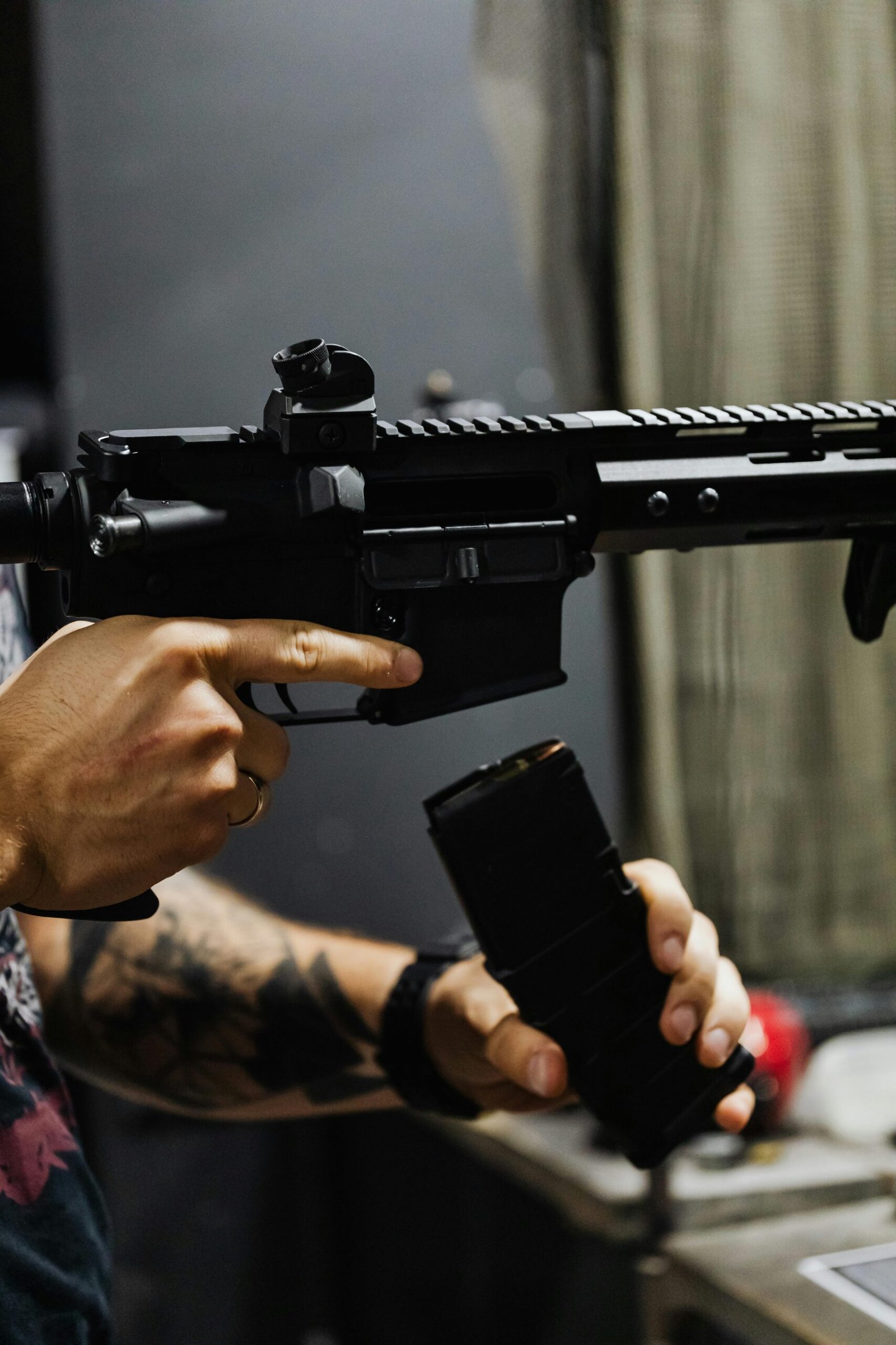Hands reloading a rifle with a magazine inside a dimly lit room.