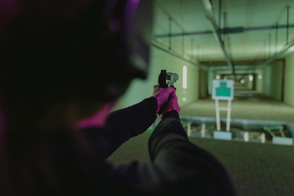 An individual targets a silhouette at an indoor shooting range using a handgun.